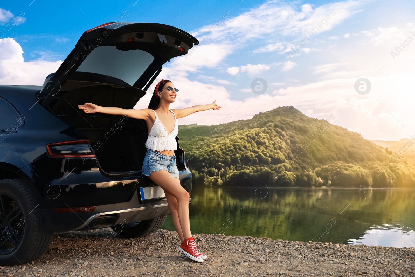 Image of Happy woman sitting in trunk of modern car in mountains