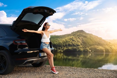 Image of Happy woman sitting in trunk of modern car in mountains