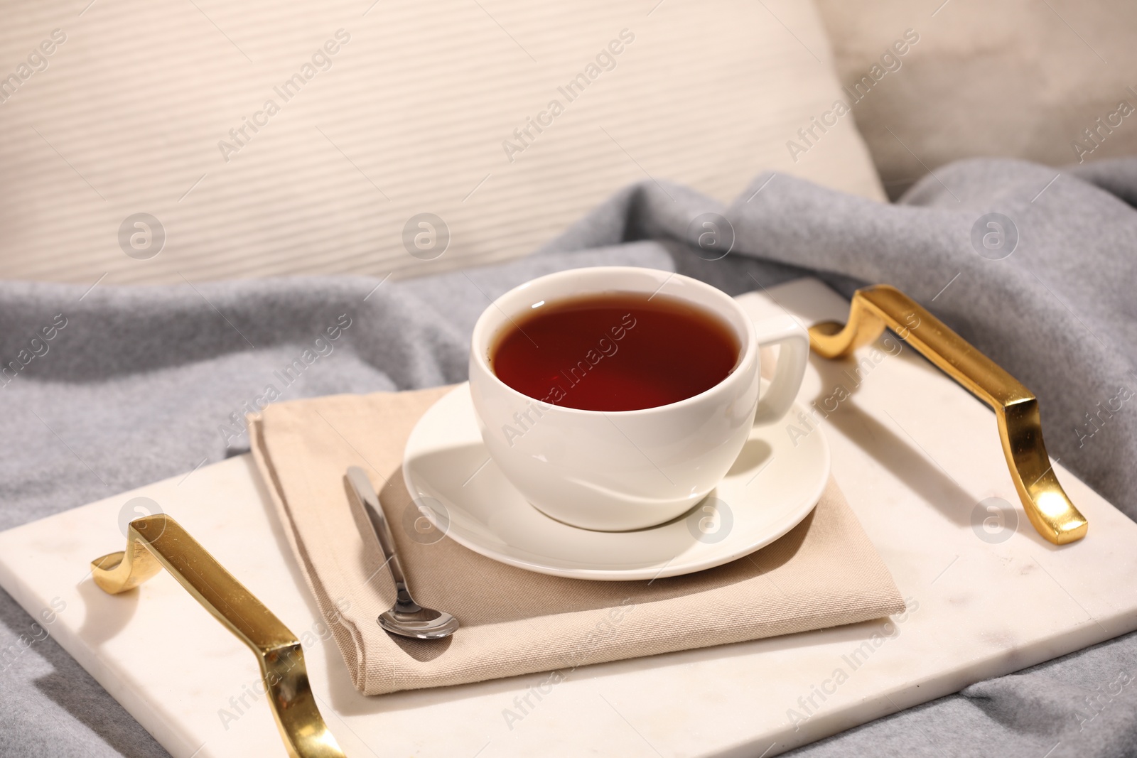 Photo of Aromatic tea in cup, saucer and spoon on bed