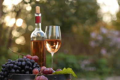 Photo of Delicious wine and ripe grapes on wooden barrel outdoors, space for text