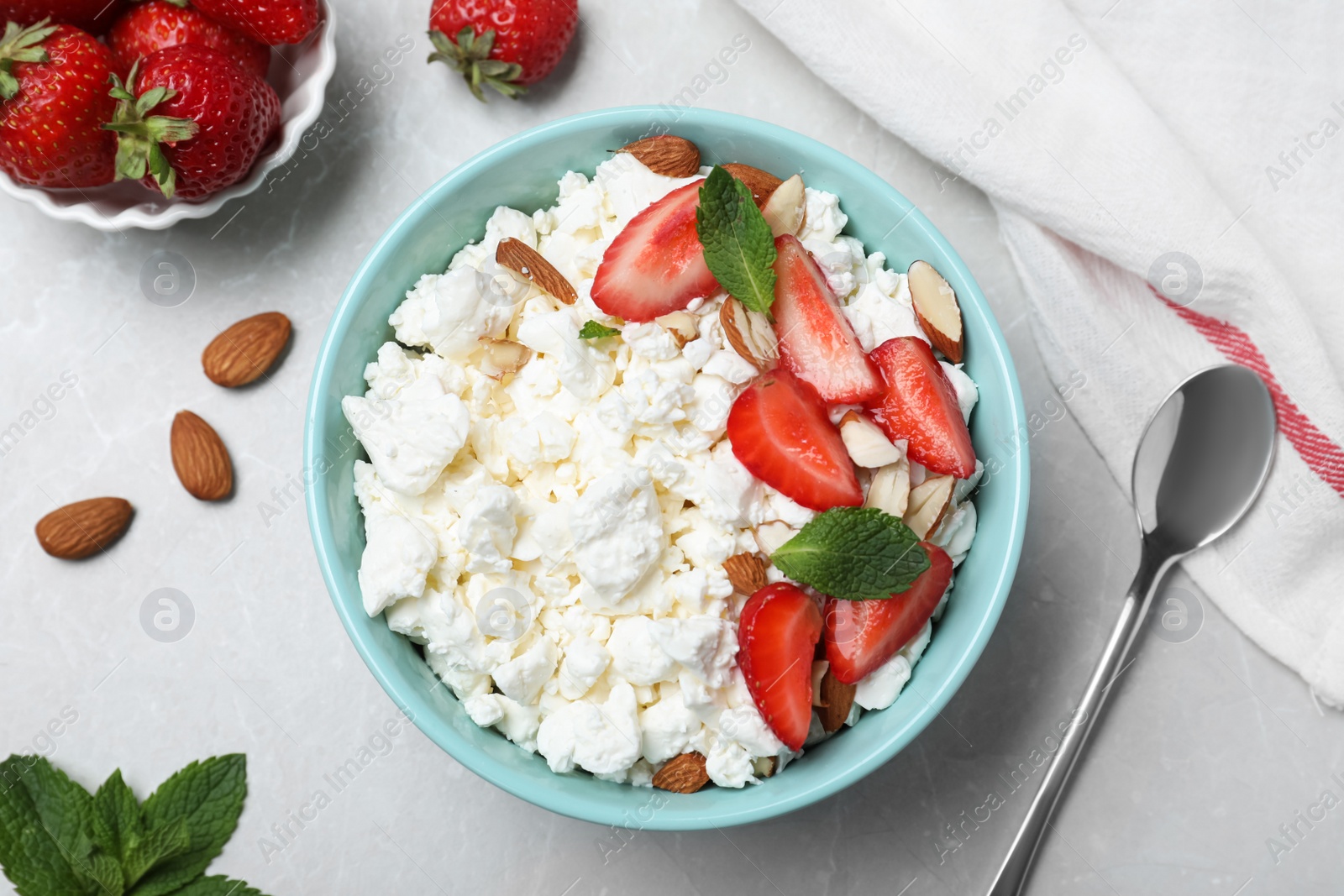 Photo of Fresh cottage cheese with strawberry and almond in bowl on light marble table, flat lay