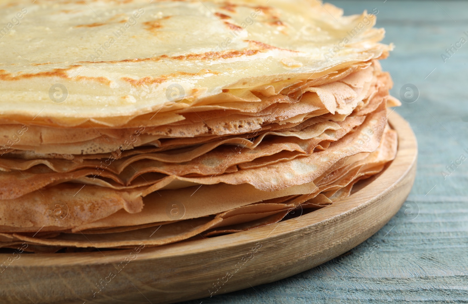 Photo of Stack of delicious crepes on blue wooden table, closeup