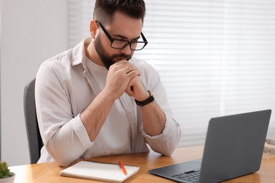 Young man in glasses watching webinar at table in room