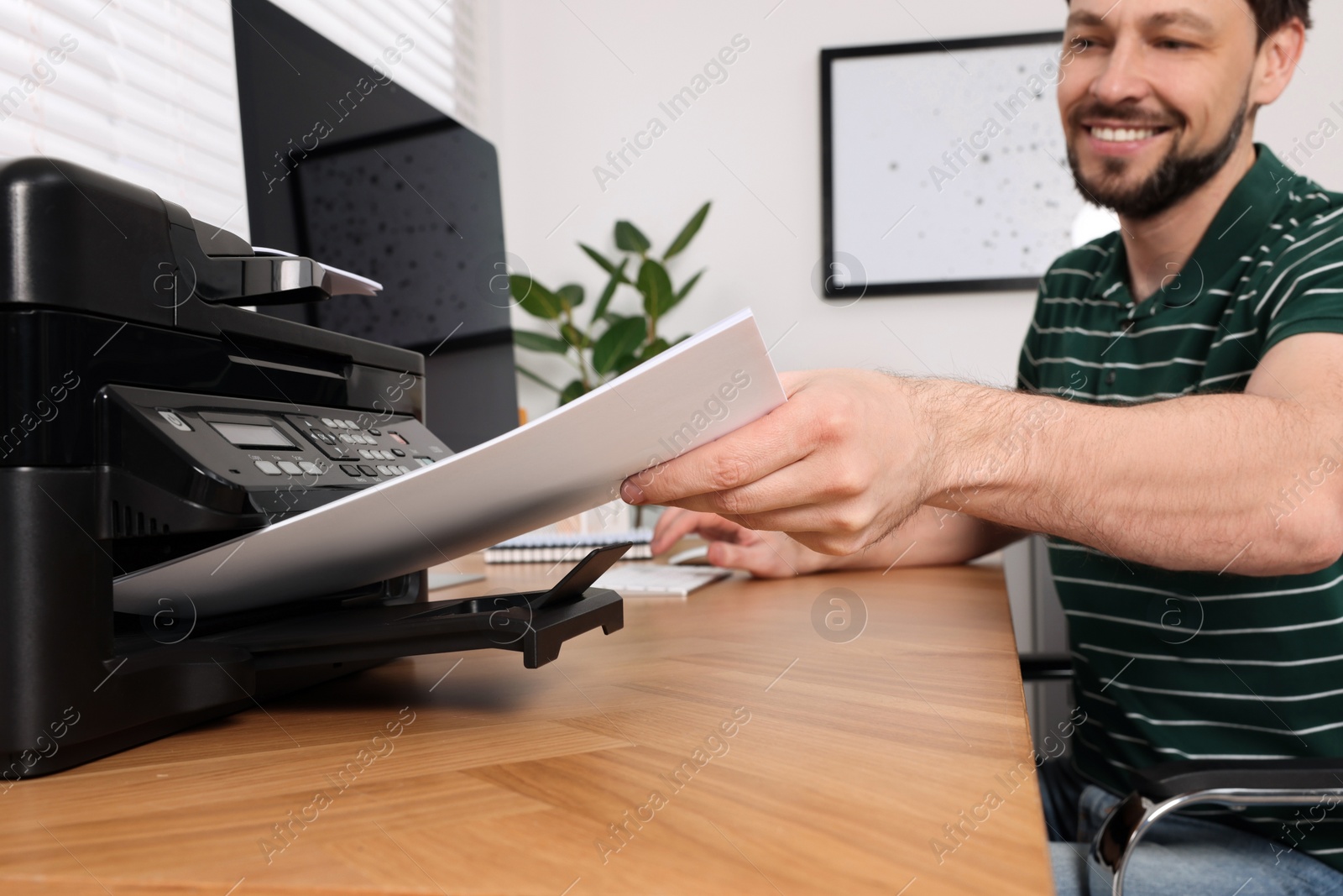 Photo of Man using modern printer at wooden table indoors, selective focus