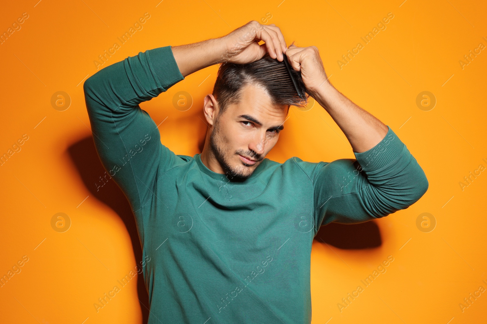 Photo of Young man with comb posing on color background. Trendy hairstyle