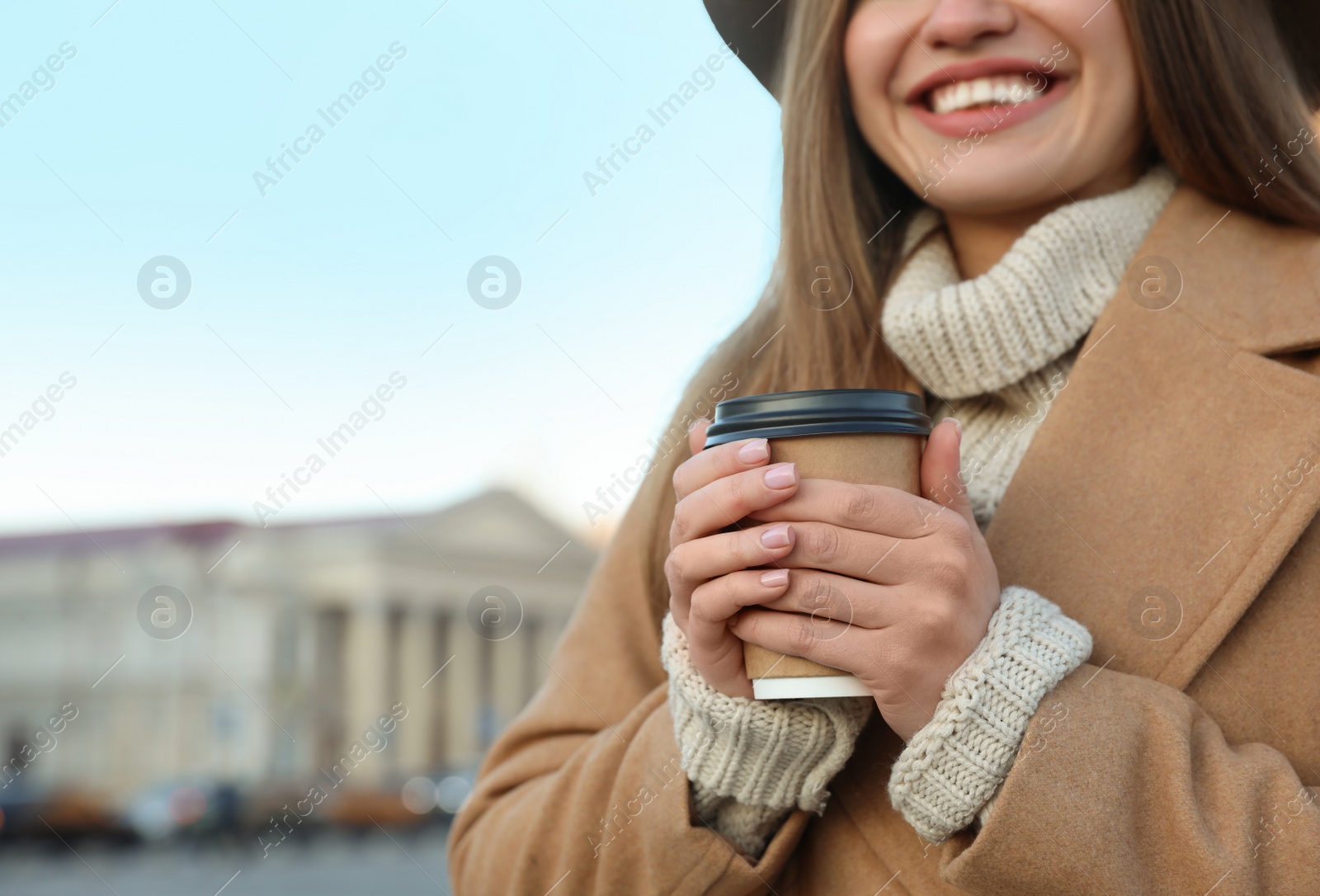 Photo of Young woman with cup of coffee on city street in morning, closeup