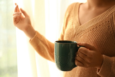 Photo of Woman holding elegant cup with tea near window indoors, closeup