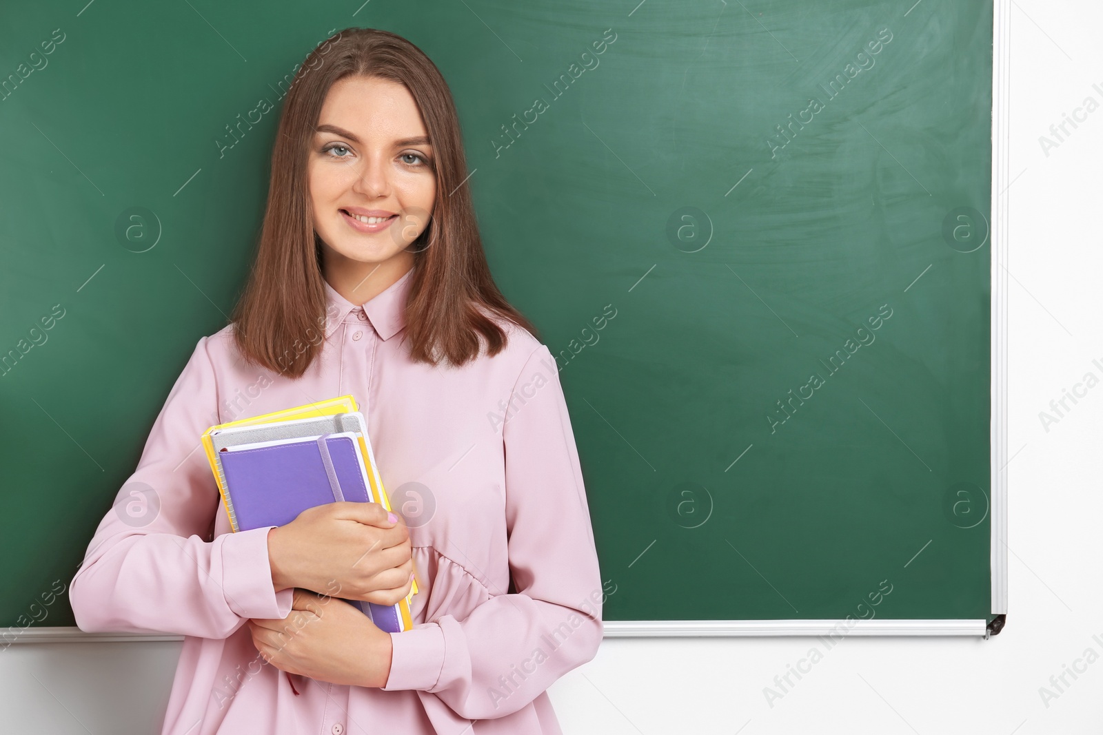 Photo of Portrait of female teacher with notebooks near chalkboard in classroom