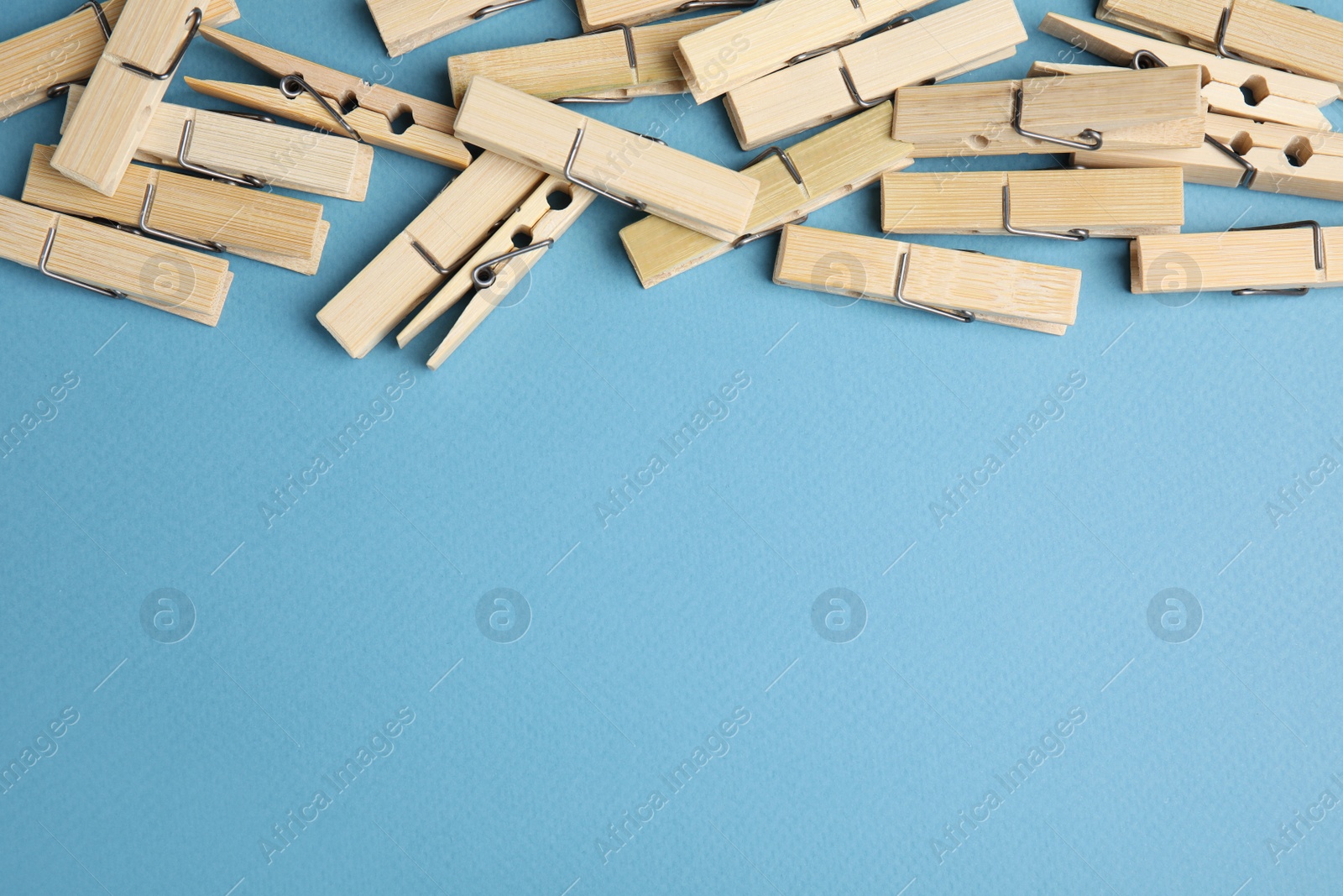 Photo of Many wooden clothespins on light blue background, flat lay. Space for text