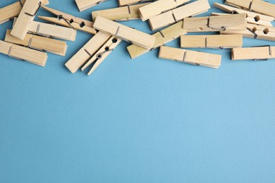 Photo of Many wooden clothespins on light blue background, flat lay. Space for text