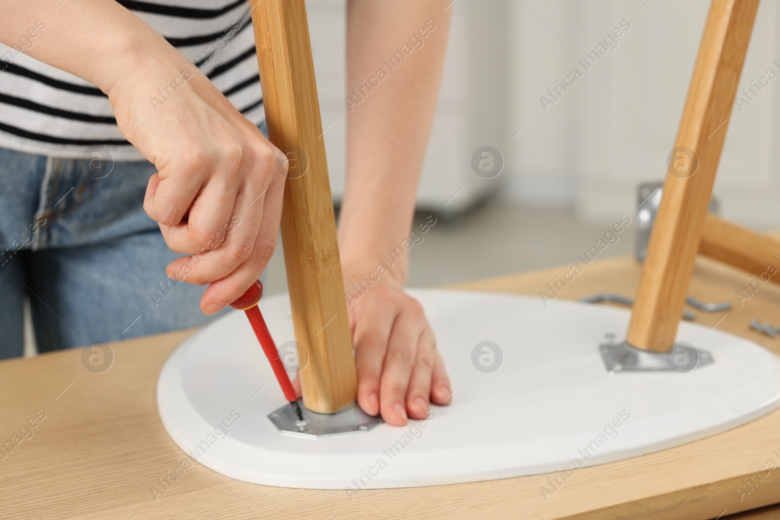 Photo of Woman with screwdriver assembling stool at table indoors, closeup