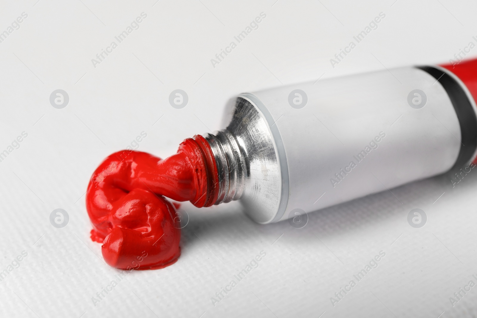 Photo of Tube with red oil paint on blank canvas, closeup