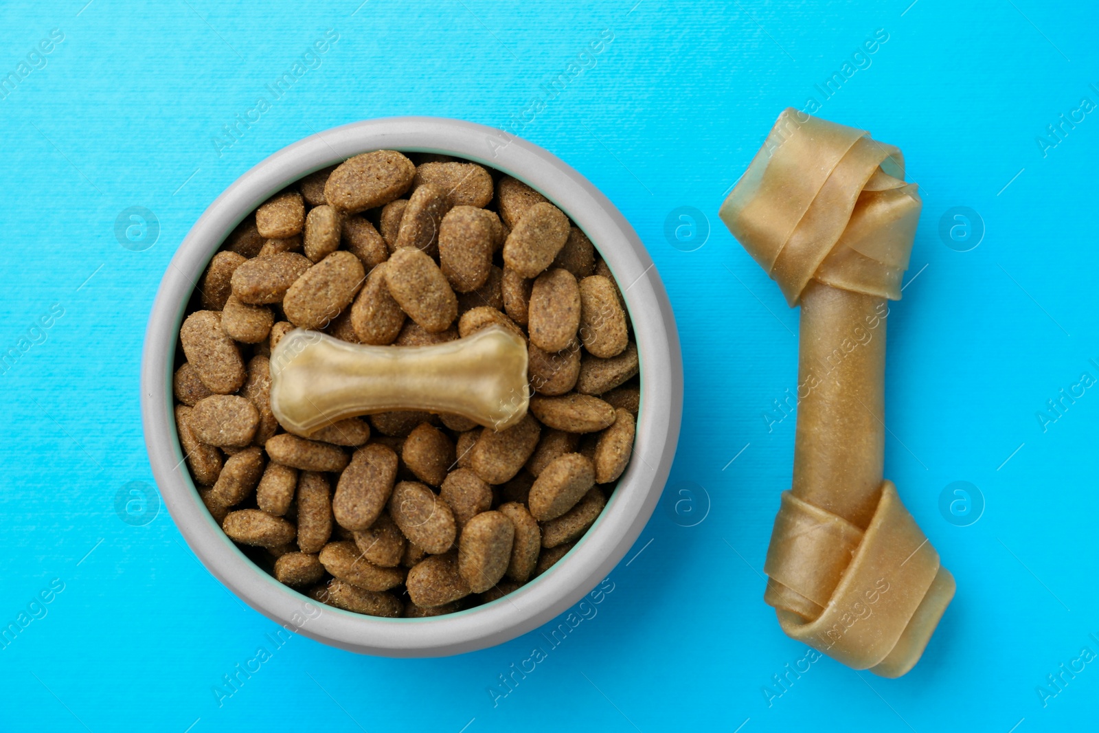 Photo of Chew bones and dry dog food on light blue background, flat lay