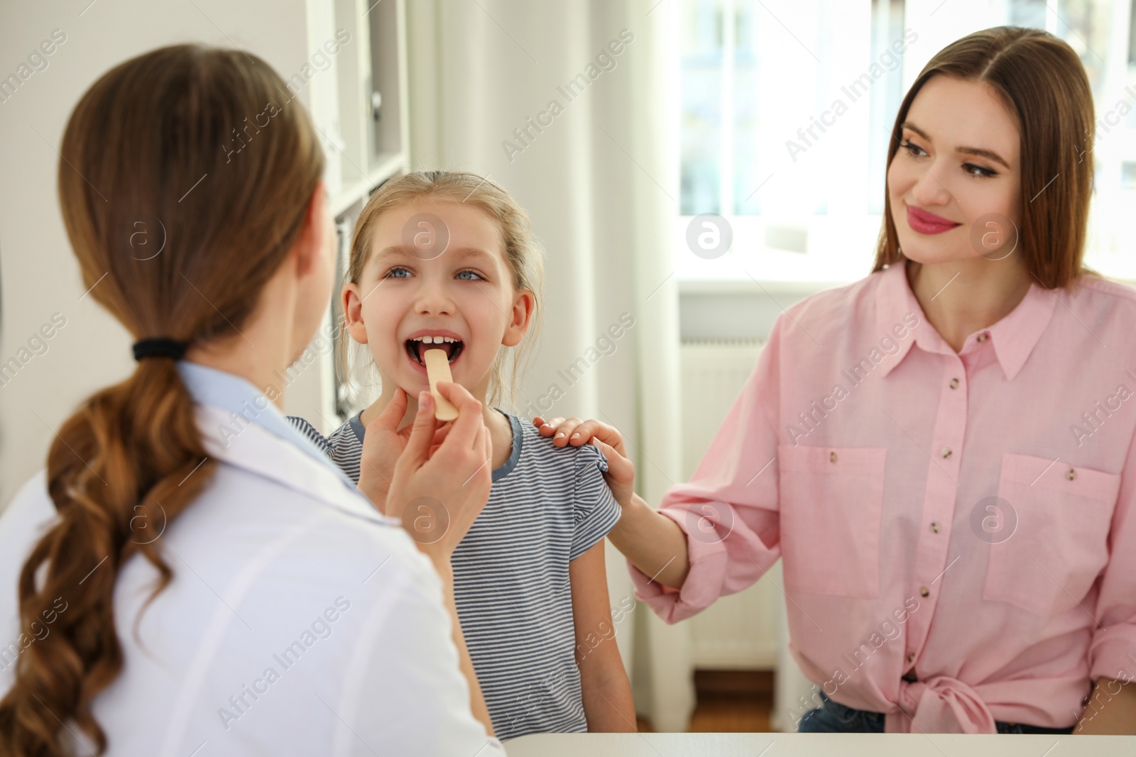 Photo of Mother and daughter visiting pediatrician. Doctor examining little patient's throat in hospital