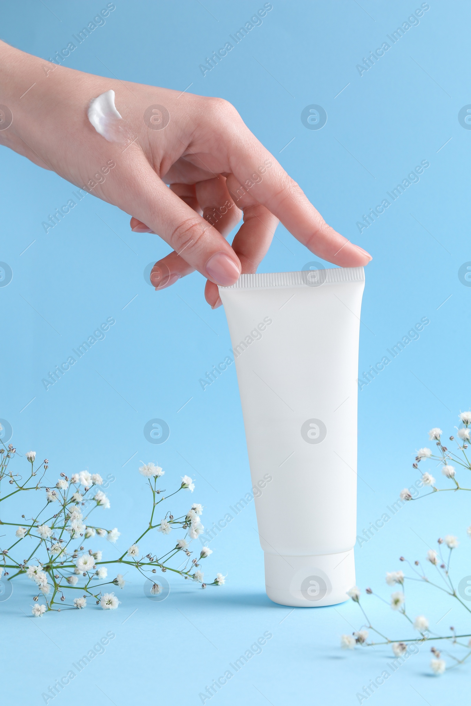 Photo of Woman with tube of cream and flowers on light blue background, closeup