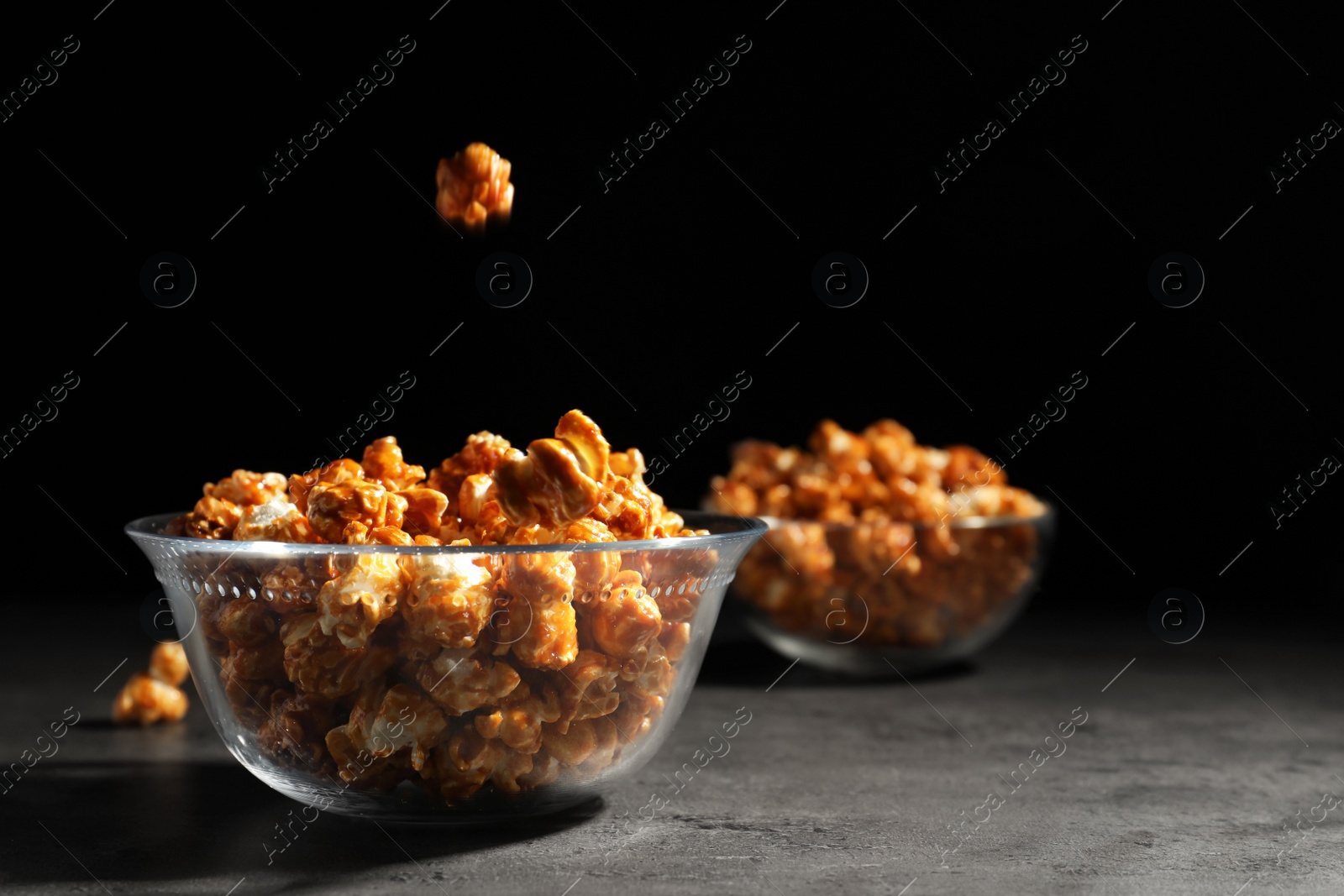 Photo of Tasty popcorn falling into bowl on table against black background. Space for text