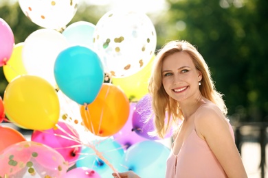 Young woman with colorful balloons outdoors on sunny day