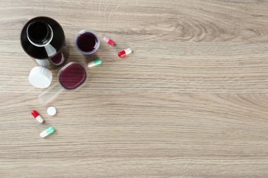 Flat lay composition with cough syrup and pills on wooden background. Space for text