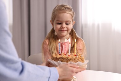 Birthday celebration. Mother holding tasty cake with burning candles near her daughter indoors