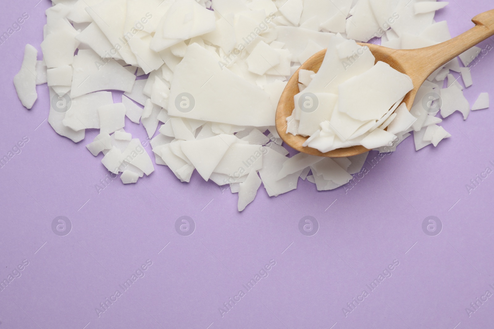 Photo of Wooden spoon and soy wax flakes on violet background, flat lay with space for text. Homemade candle material