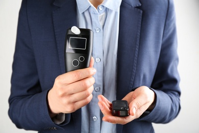 Woman holding modern breathalyzer and car key on light background, closeup