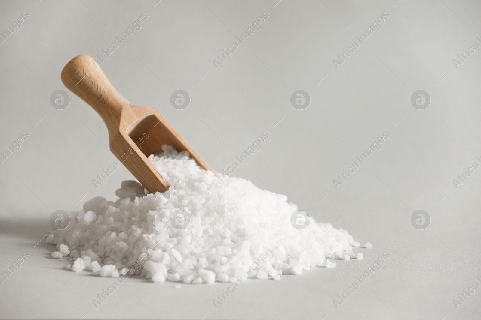 Photo of Organic salt and wooden scoop on light grey background. Space for text