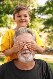 Photo of Senior man with his little grandson having fun together in park