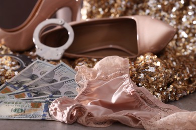 Prostitution concept. Women's panties, dollar banknotes, handcuffs and high heeled shoes on grey textured background, selective focus