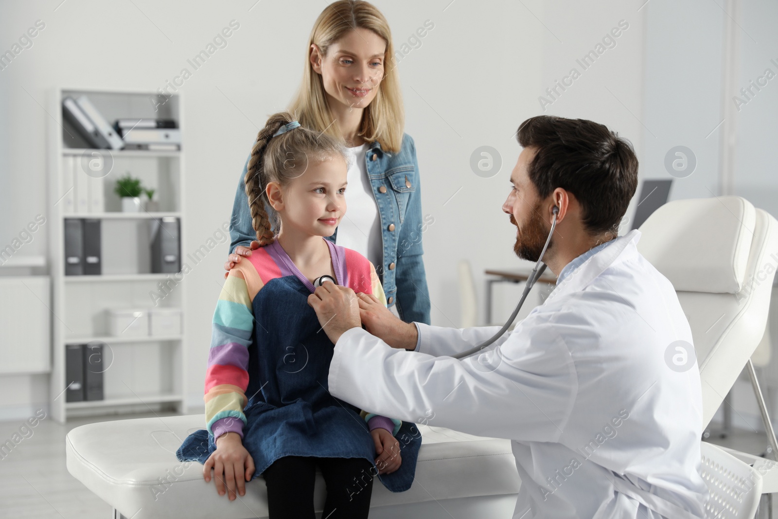 Photo of Mother and daughter having appointment with doctor. Pediatrician examining patient with stethoscope in clinic