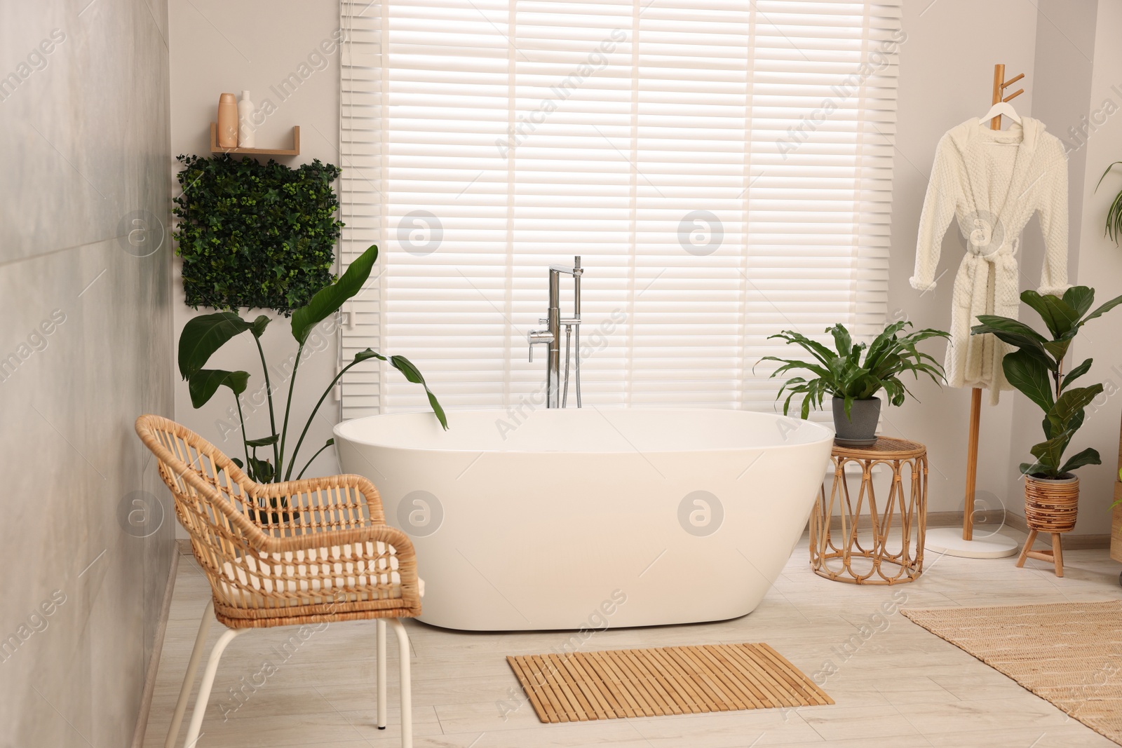 Photo of Green artificial plants, robe and tub in bathroom