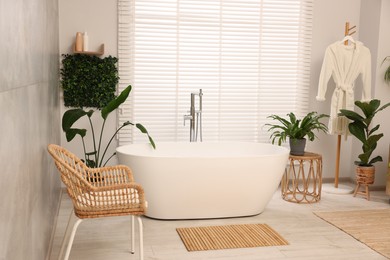 Photo of Green artificial plants, robe and tub in bathroom