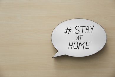 Photo of Top view of speech bubble with hashtag STAY AT HOME on wooden background, space for text. Message to promote self-isolation during COVID‑19 pandemic
