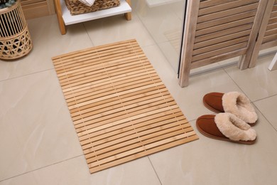 Photo of Wooden mat and slippers on tiled floor in bathroom. Stylish accessory