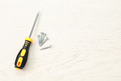 Screwdriver with yellow handle and screws on white wooden table, flat lay. Space for text