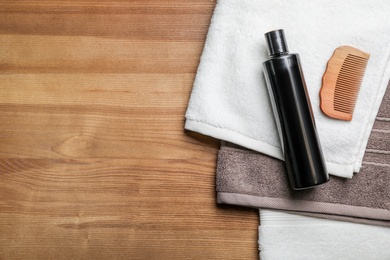 Photo of Bottle of shampoo, towels and comb on wooden background, top view with space for text