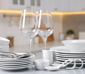 Photo of Set of clean dishware, glasses and cutlery on table in kitchen