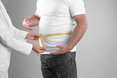 Photo of Doctor measuring fat man's waist on grey background. Weight loss