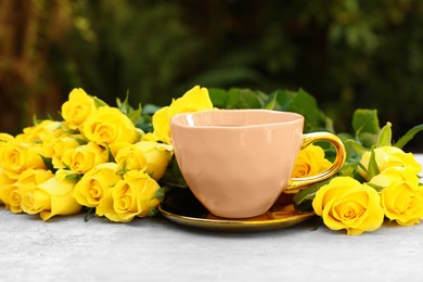 Cup of drink and beautiful yellow roses on light table outdoors