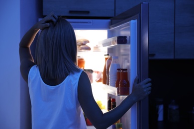 Woman looking into refrigerator full of products at night