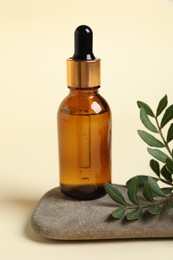 Bottle with cosmetic oil, stone and green leaves on beige background