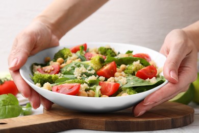 Photo of Healthy meal. Woman putting bowl of tasty salad with quinoa, chickpeas and vegetables on table, closeup