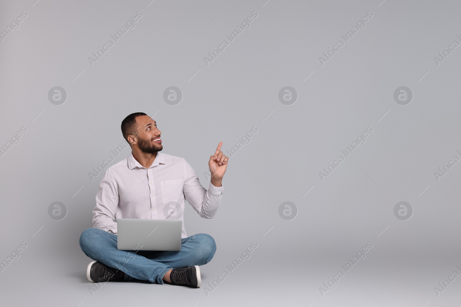 Photo of Smiling young man with laptop on grey background, space for text