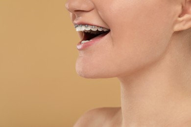 Happy woman with dental braces on brown background, closeup. Space for text