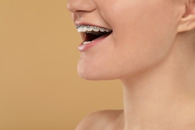 Photo of Happy woman with dental braces on brown background, closeup. Space for text