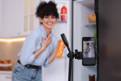 Photo of Food blogger recording video in kitchen, focus on smartphone