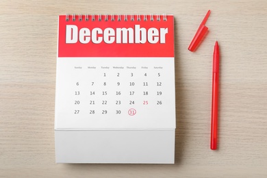 Photo of Calendar with marked date and pen on wooden table, flat lay. New Year countdown
