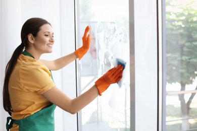 Photo of Young woman cleaning window glass at home