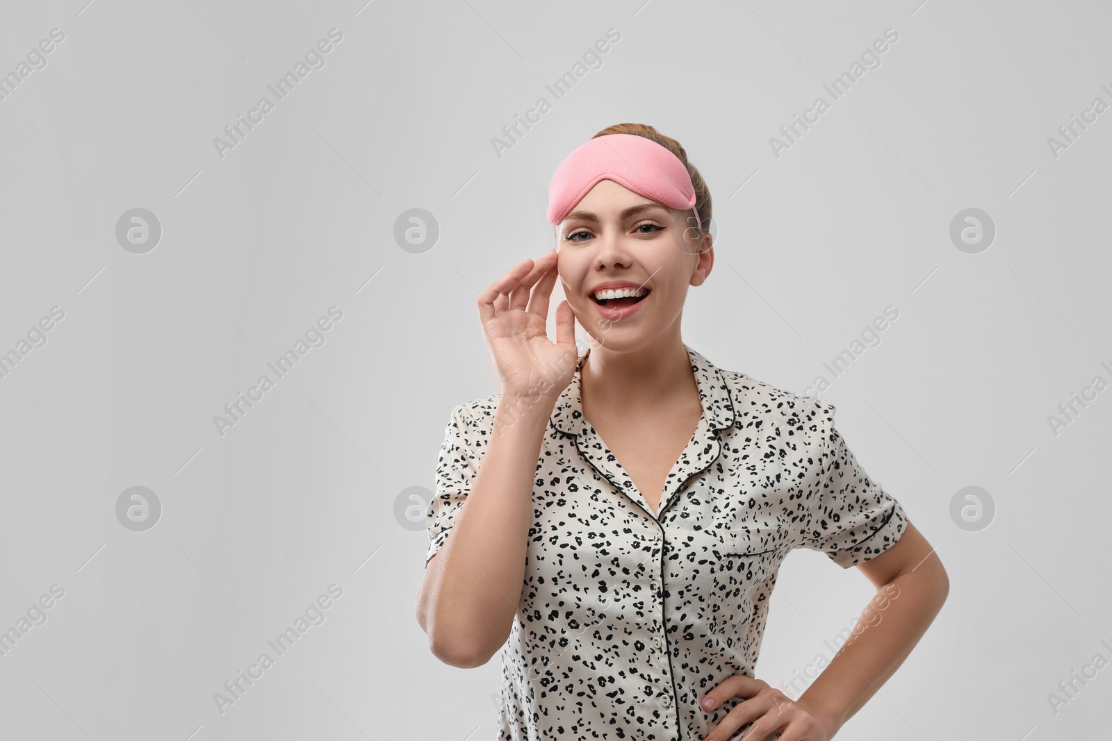 Photo of Beautiful woman wearing pajamas and sleeping mask on light grey background. Bedtime