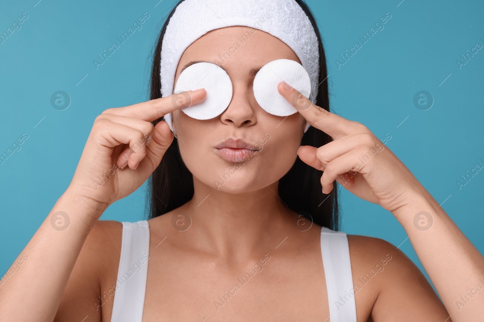 Photo of Young woman covering her eyes with cotton pads on light blue background