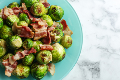 Photo of Delicious Brussels sprouts with bacon on white marble table, top view